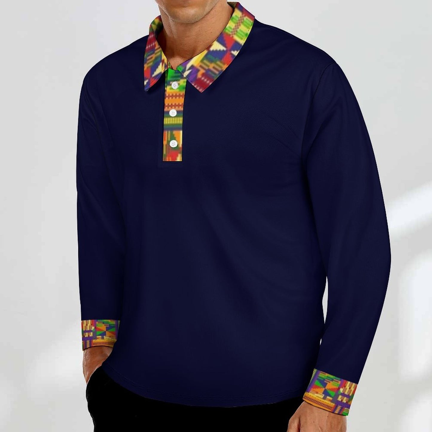 A man wearing a navy blue long-sleeve polo shirt with a colorful patterned collar and matching patterned button placket, paired with black pants against a light gray background.