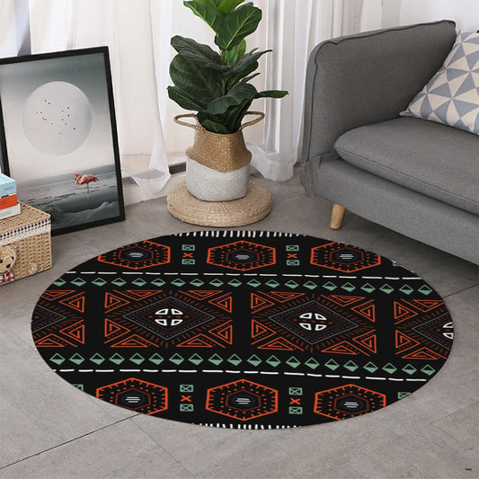 A round area rug with a black background and a colorful geometric tribal pattern in orange, green, and white, styled in a modern living room next to a gray sofa and a potted plant.