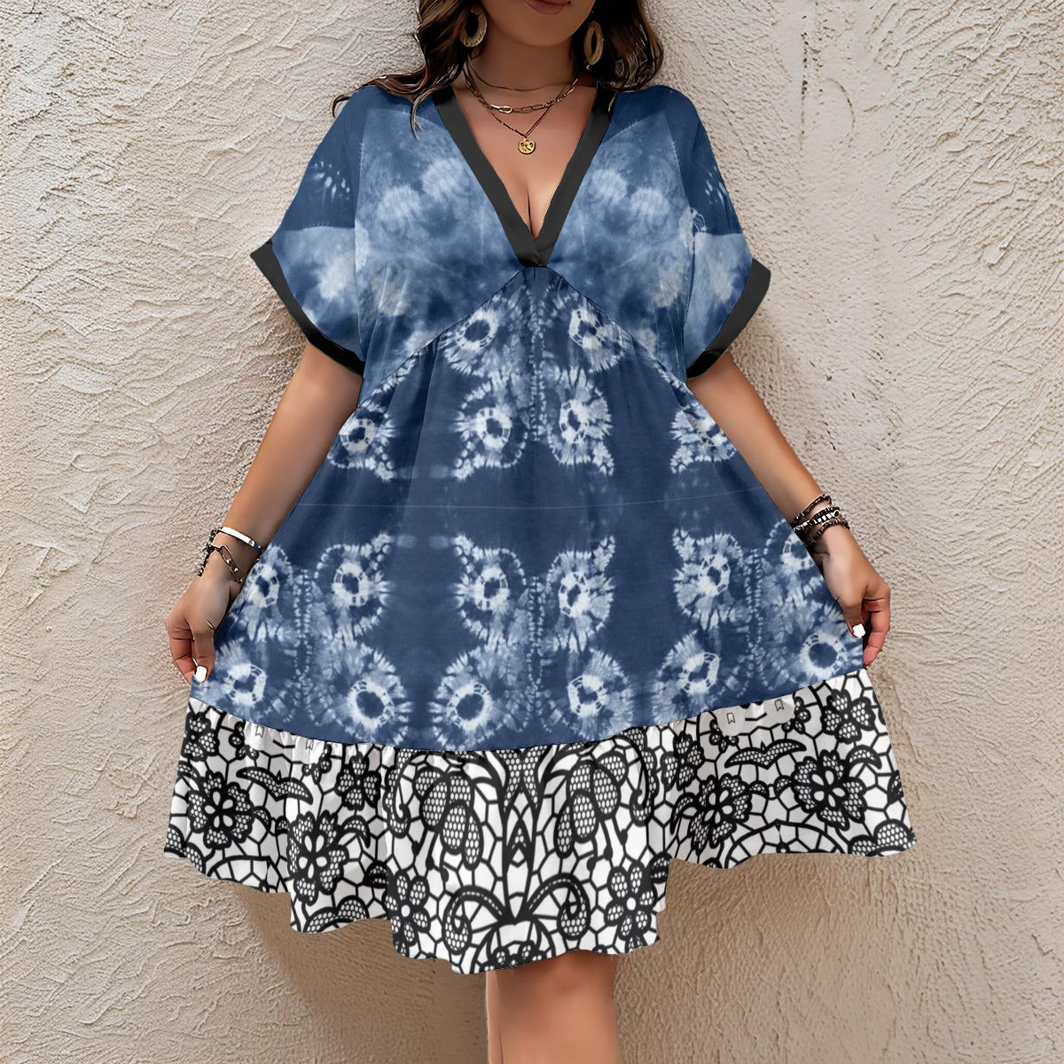A woman wearing a blue and white tie-dye dress with a black and white patterned hem, standing against a textured beige stucco wall.