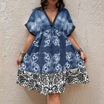 A woman wearing a blue and white tie-dye dress with a black and white patterned hem, standing against a textured beige stucco wall.