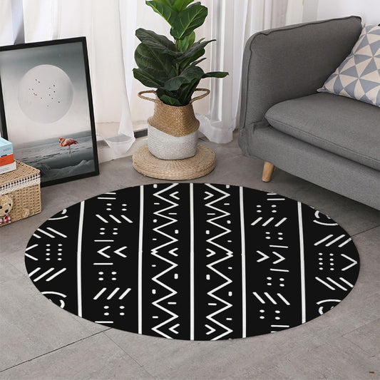 A round area rug with a black background and a colorful geometric tribal pattern in black and white, styled in a modern living room next to a gray sofa and a potted plant.