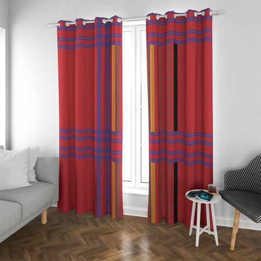 A pair of red grommet curtains with blue, purple, and orange striped patterns hanging on a white rod in a bright room with a window, gray sofa, and wooden floor.