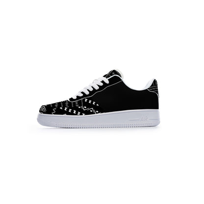 A black low-top sneaker with white laces, a white midsole, and white geometric tribal-style patterns printed on the toe box and heel.