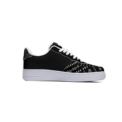 A black low-top sneaker with white geometric tribal patterns on the toe box and heel, white laces, and a thick white rubber sole, shown in a side profile on a white background.