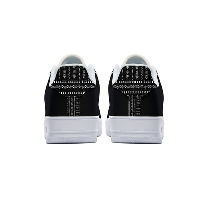 A pair of black and white low-top sneakers shown from the back, featuring a black canvas upper with white geometric patterned details and thick white rubber soles.