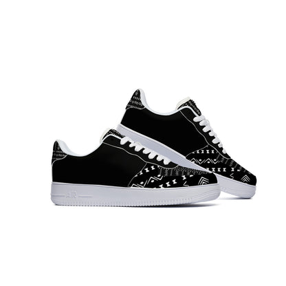 A pair of black low-top sneakers with white geometric tribal-style patterns on the toe box and heel, featuring white laces and white midsoles, shown against a plain white background.