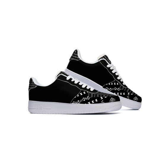 A pair of black low-top sneakers with white geometric tribal-style patterns on the toe box and heel, featuring white laces and white midsoles, shown against a plain white background.