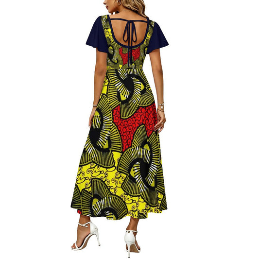 A woman modeling a short-sleeve maxi dress from the back, featuring a navy blue back panel with tie straps and a vibrant African wax print skirt in yellow, black, and red.