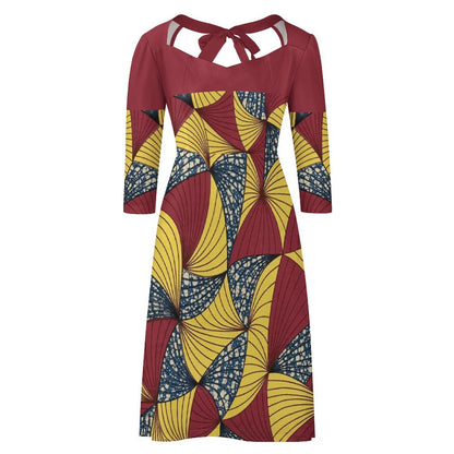 A three-quarter sleeve cold-shoulder dress featuring a geometric African wax print with red, yellow, and navy blue fan-like patterns, set against a plain white background.