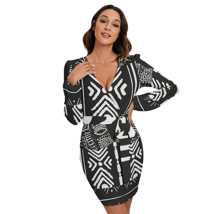A woman modeling a black and white geometric patterned mini dress with long sleeves, a deep V-neckline, and a matching self-tie belt, set against a plain white background.